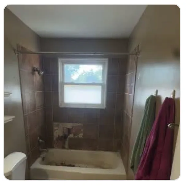 Dark brown tiled tub surround with an old alcove tub and window