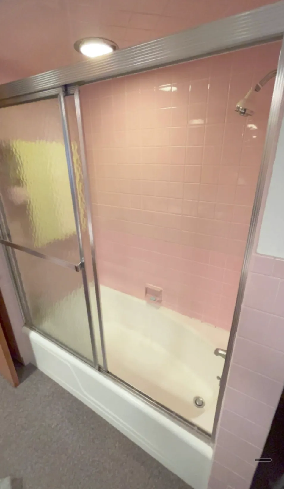Older bathroom with pink square tile, tub, and frosted sliding shower door