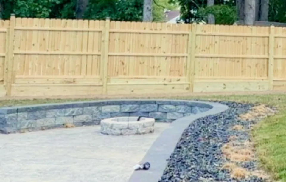 New cedar privacy fence with a curved stone retaining wall, fire pit, and gravel patio